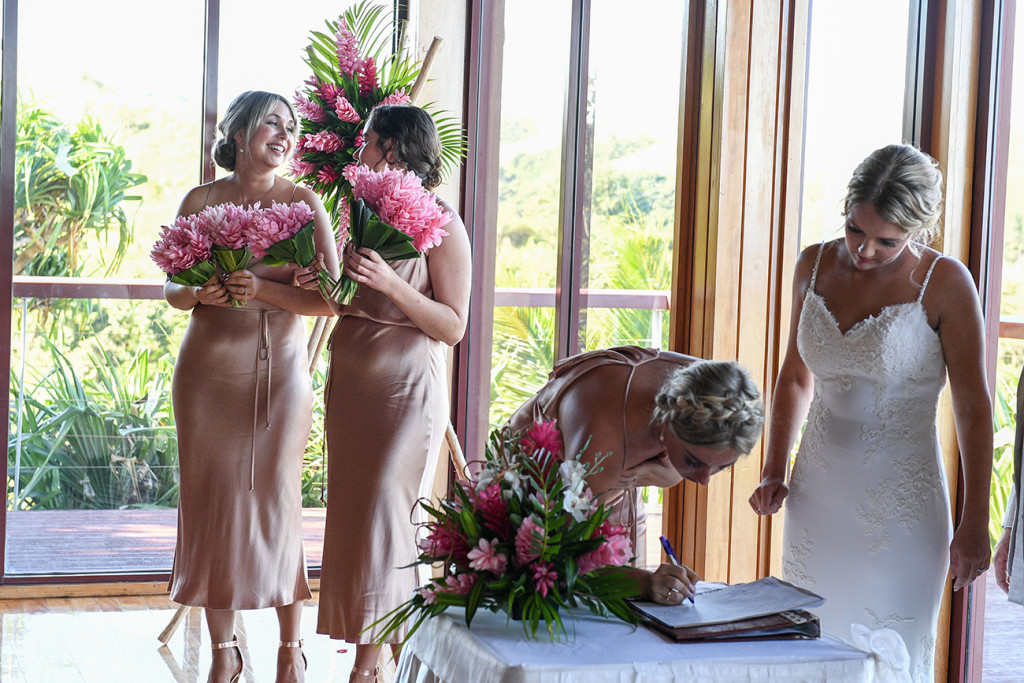 Bridesmaids watch as bride of honour signs marriage certificate