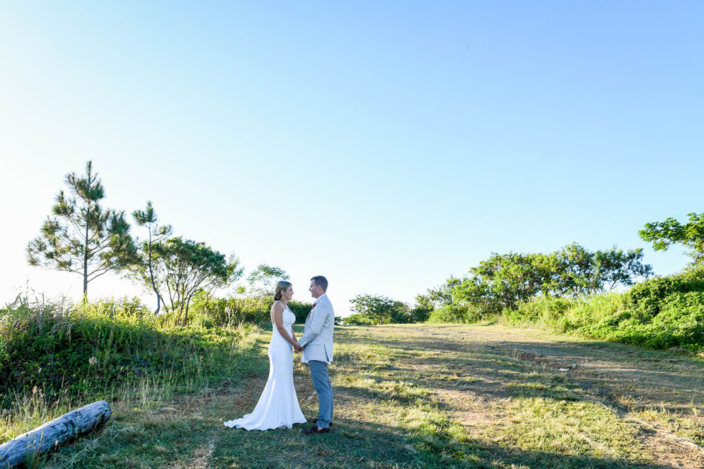 Bride and groom stand in Fiji countryside during sunset