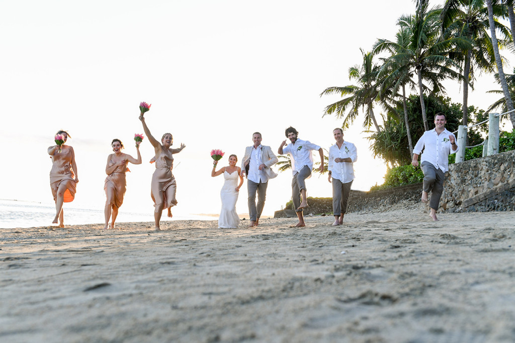 Bridal party runs on the beach during sunset