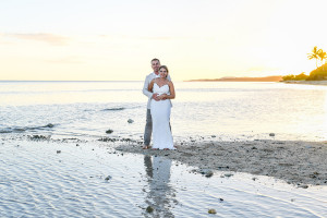Bride and groom pose barefoot in the ocean against the fiery sunset in Fiji waters