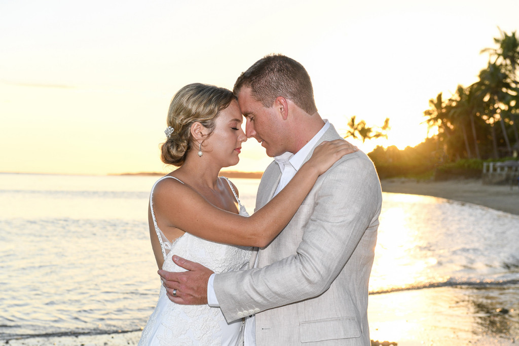 Bride and groom touche noses against fiery sunset Fiji