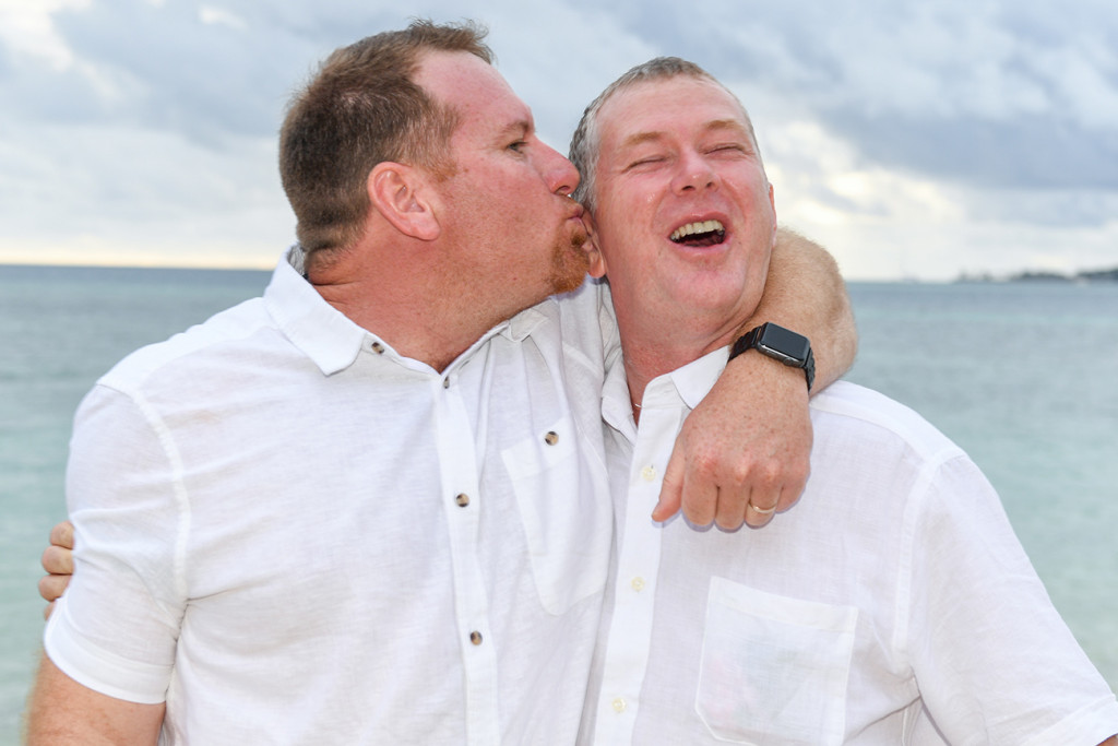 Brother kisses groom against sea
