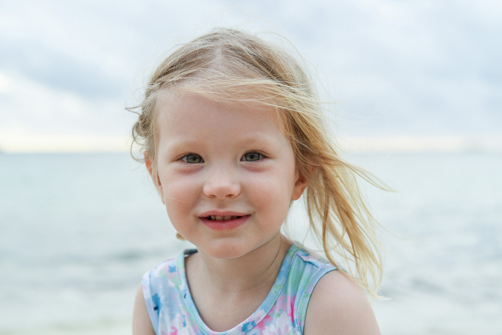 Cute blonde baby girl smiles against the sea