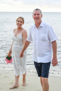 Bride and groom laugh while holding hands against sea