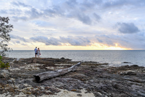Wide landscape shot of Bride and groom standing on coral rocks against fiery sunset