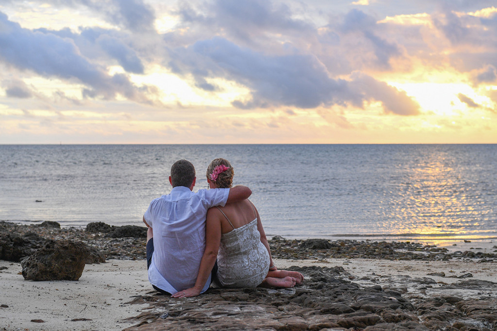 Bride and groom sit and watch sunset over the sea in Fiji Island