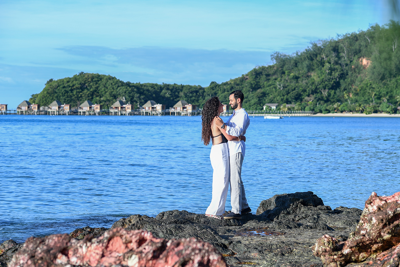 Newly married couple hug with Fiji greenery, ocean and Resort Villas in the background