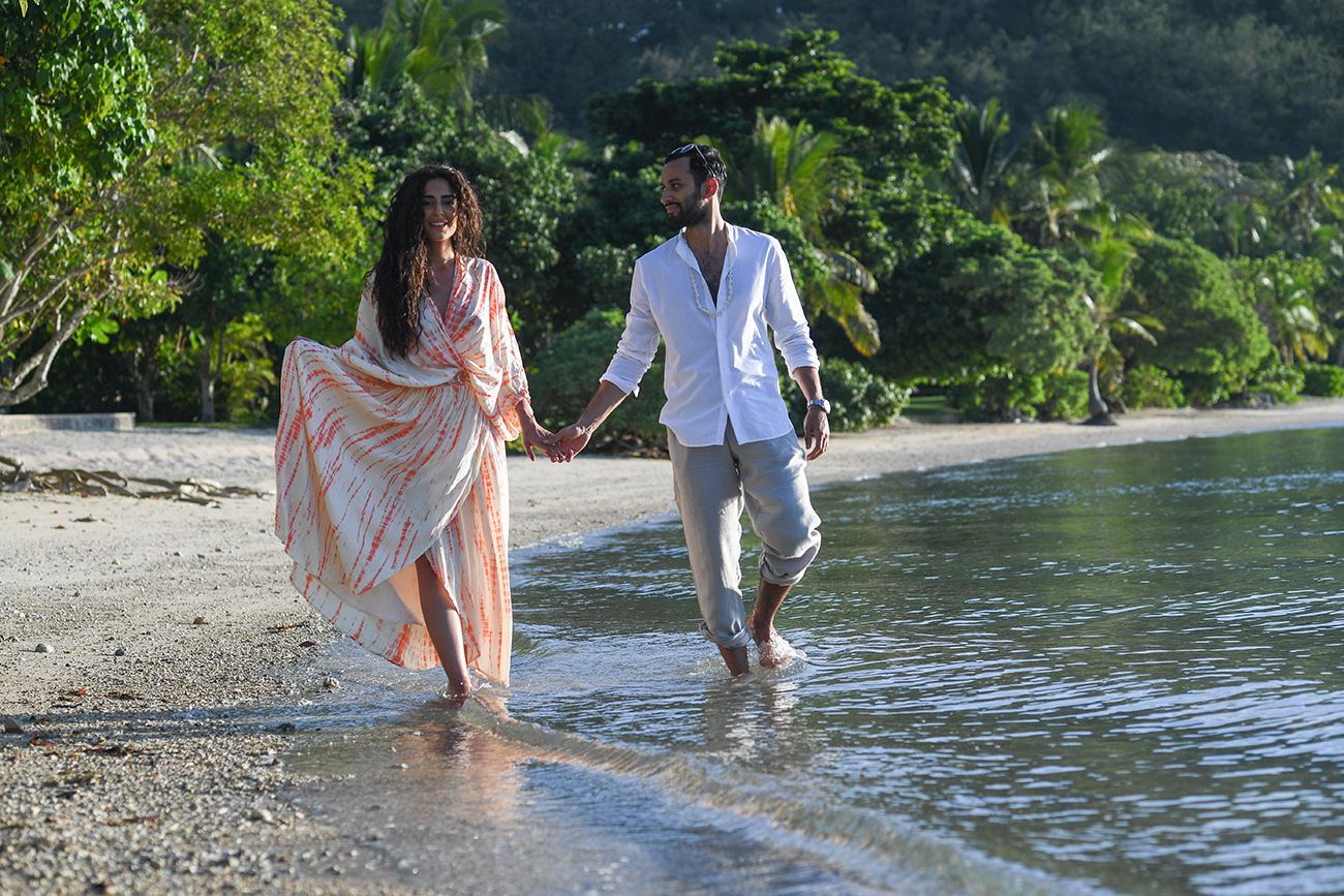 Newly wed couple hold hands as they stroll in the ocean in Likuliku Resort Fiji