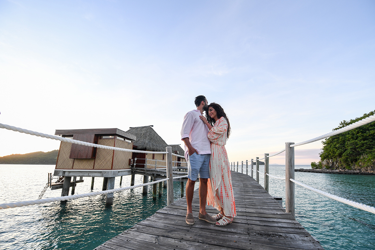 Stunning newly wed couple hug on wooden bridge at sunset Likuliku Fiji