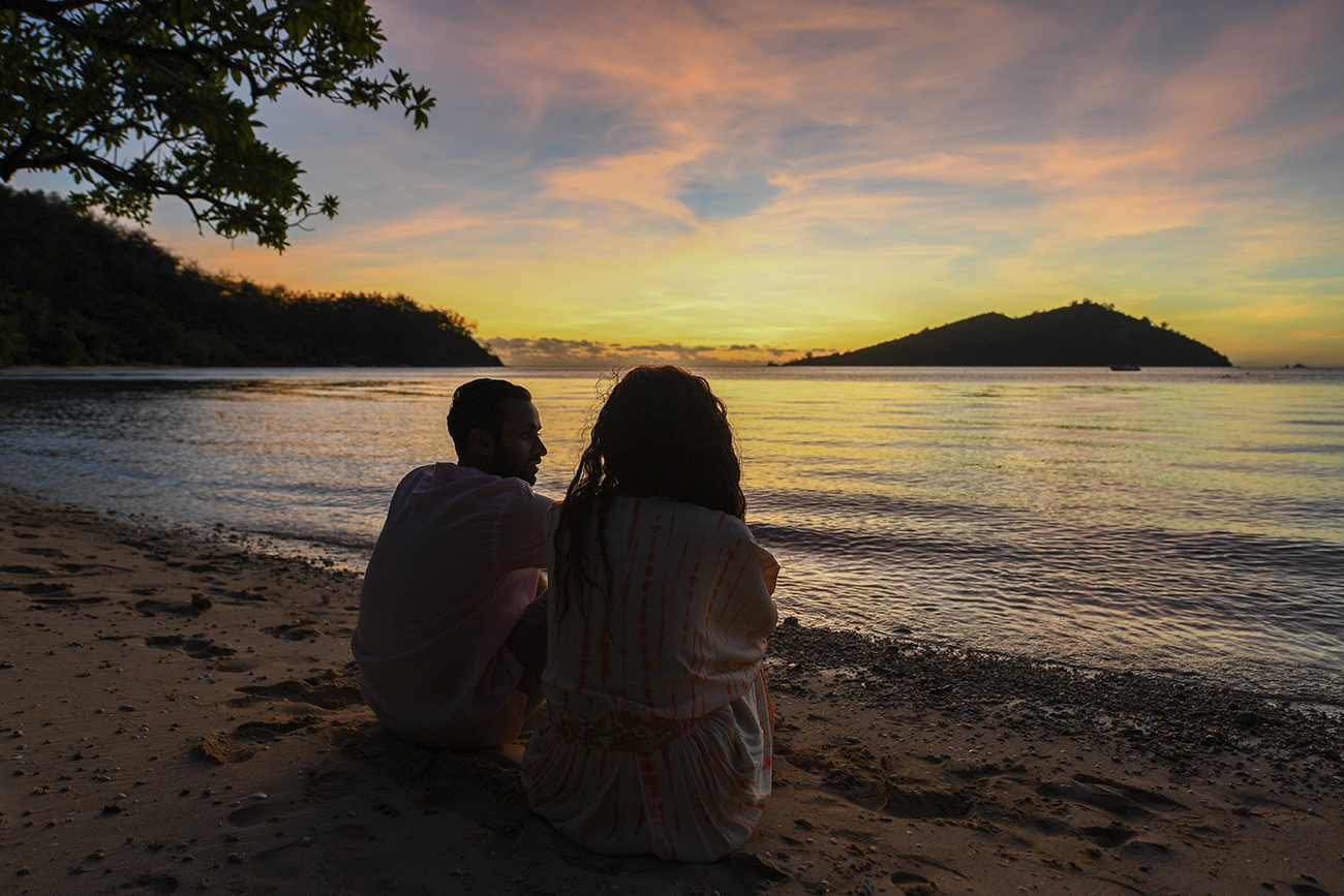 Newly wed couple sit in the sand watching the sunset in Likuliku Fiji
