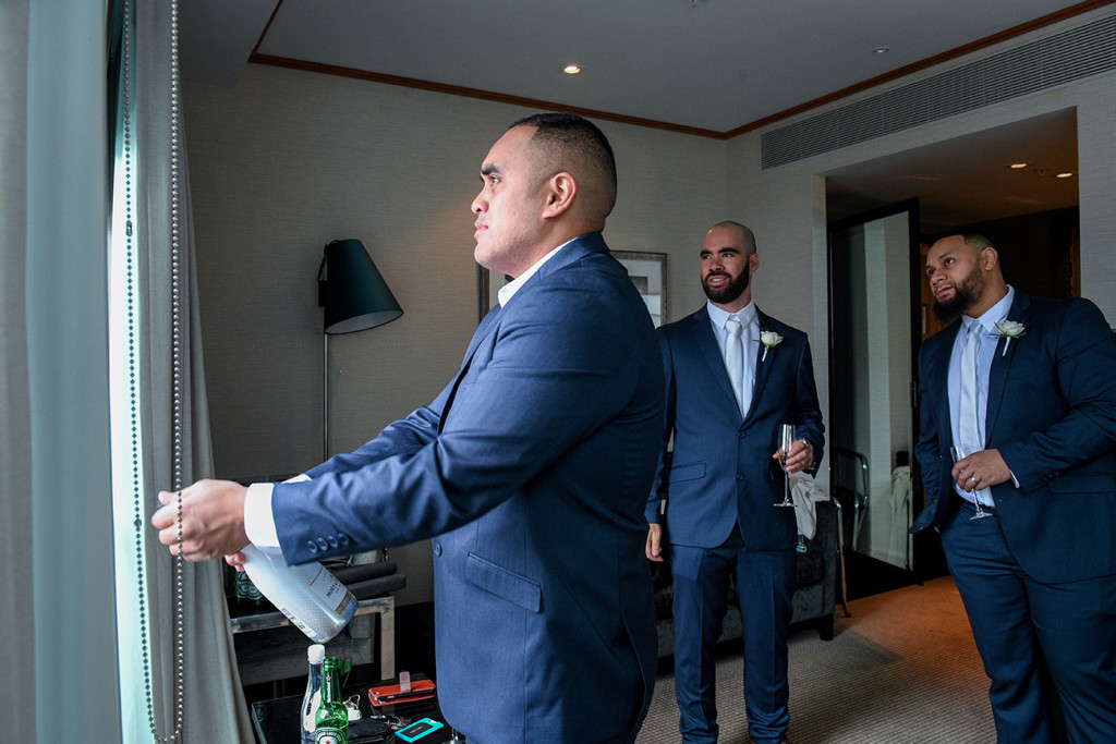 Groom pops champagne bottle open during wedding preparation in Auckland Sofitel