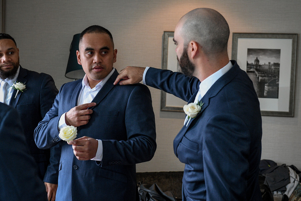 Groomsman helps groom adjust suit at wedding prep
