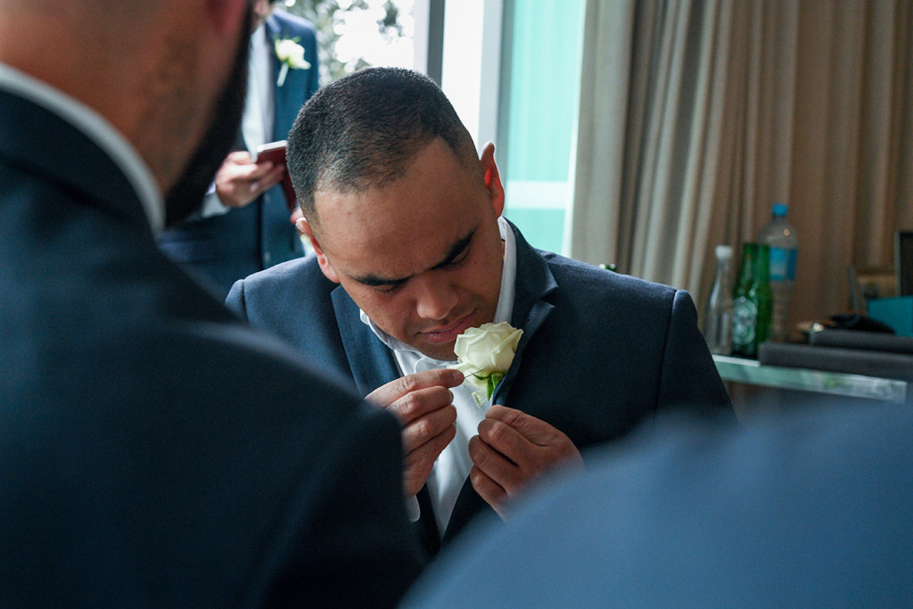 The groom adjusts his boutonniere at wedding prep