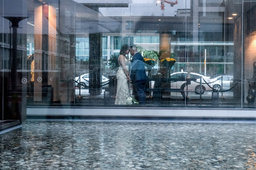 Wideshot through a glass wall of the bride and groom kissing