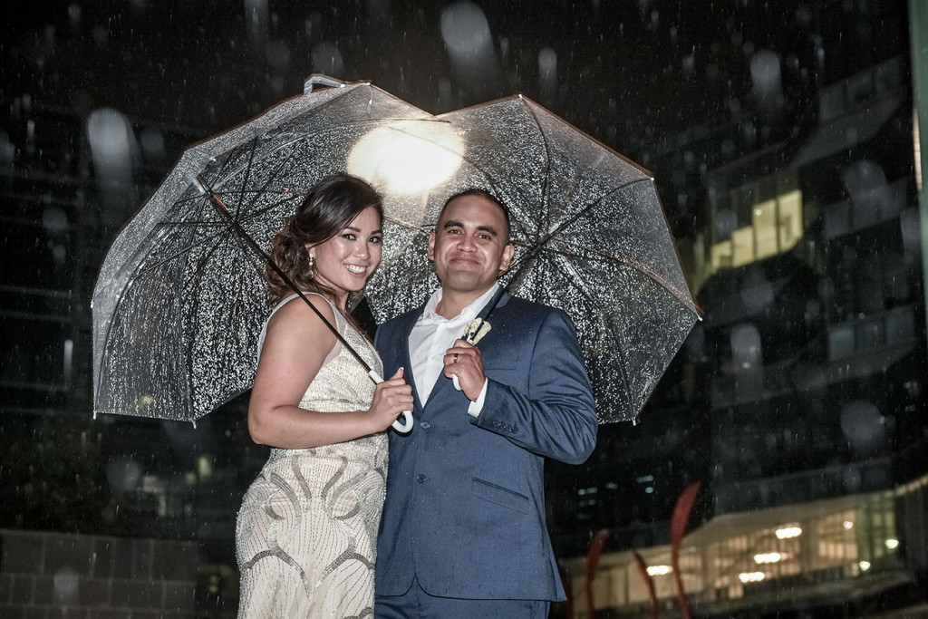 Bride and groom pose with umbrellas in the rain at night at the Viaduct