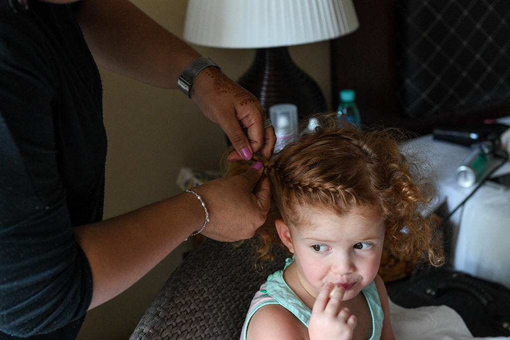 Flower girl gets a french plait in her hair during wedding preparations