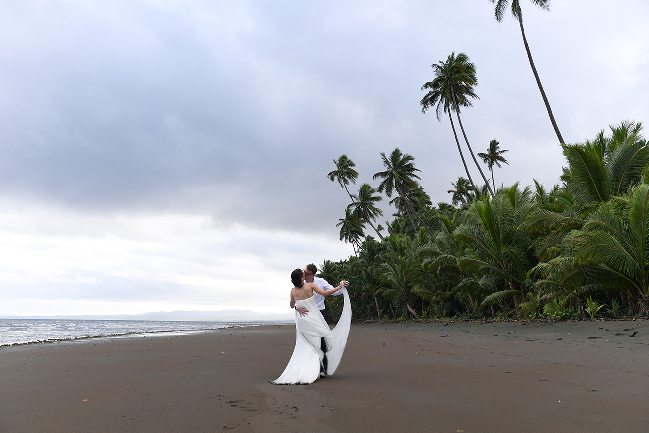 Bride and groom dance on the shore by palm trees of Fiji Island