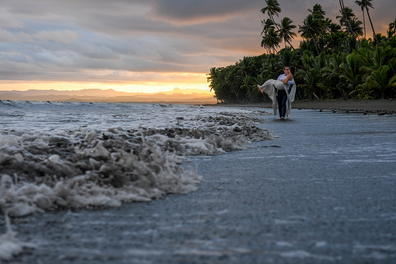 The groom carries the bride ashore during Fiji sunset