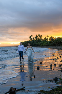 Bride and groom stroll hand in hand on the Fiji beach against the orange sunset