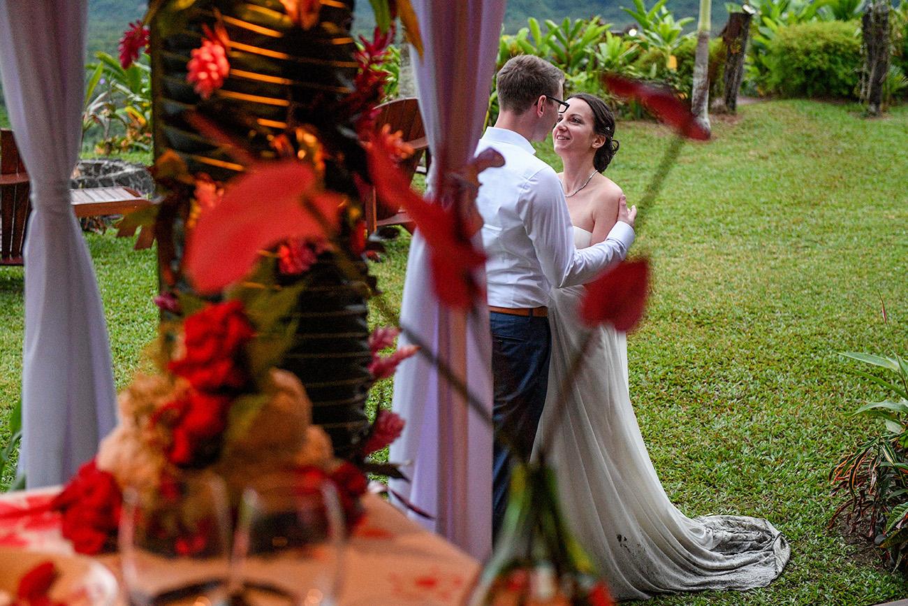 A peek through red flower bouqet of the couple at the altar
