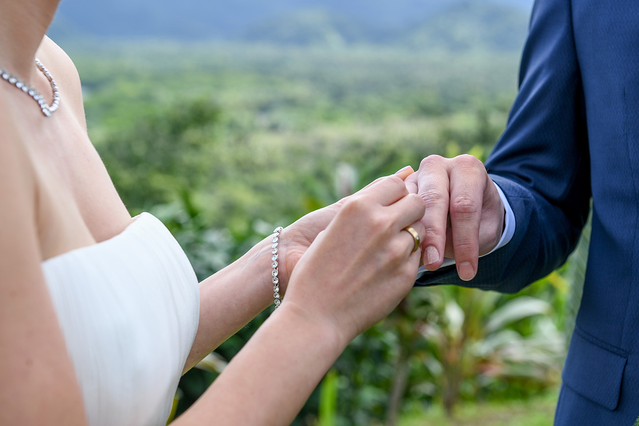 The bride slips simple gold ring on grooms finger at Fiji countryside
