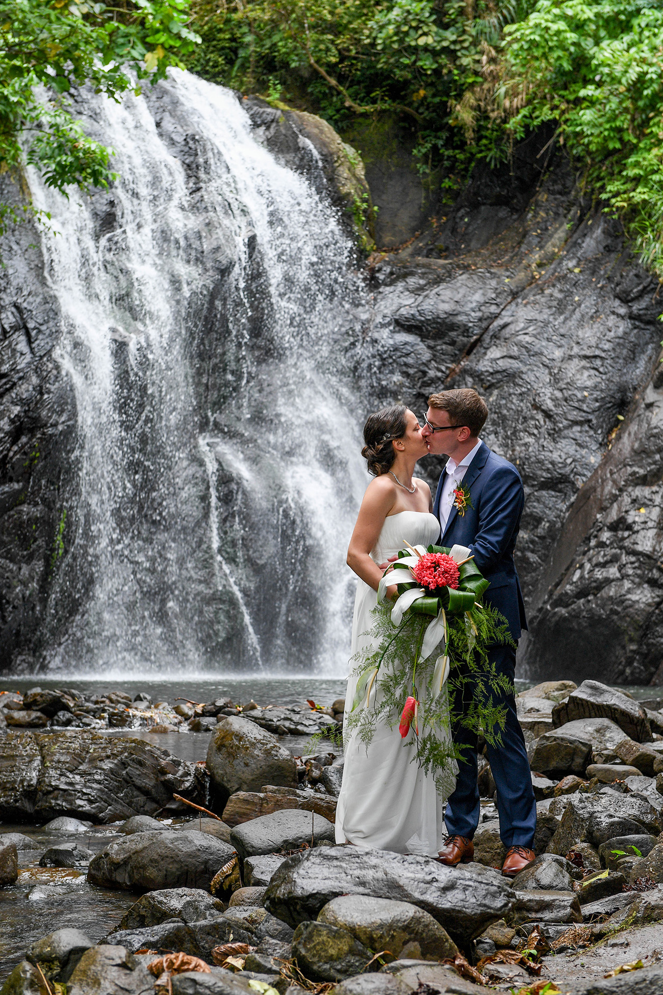 German bride and groom kiss in front of stunning waterfall