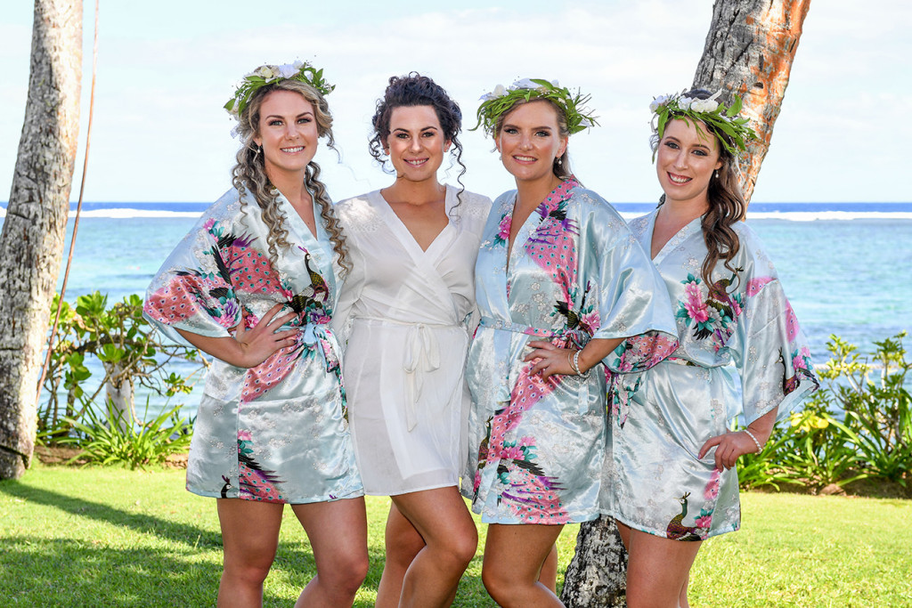 Bride poses with bridesmaids dressed in blue floral dressing gowns by the beach