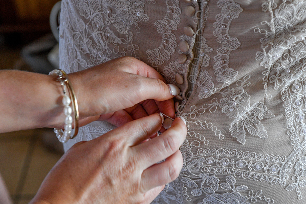 Close up detail of bride zipping up lace and pearls wedding dress