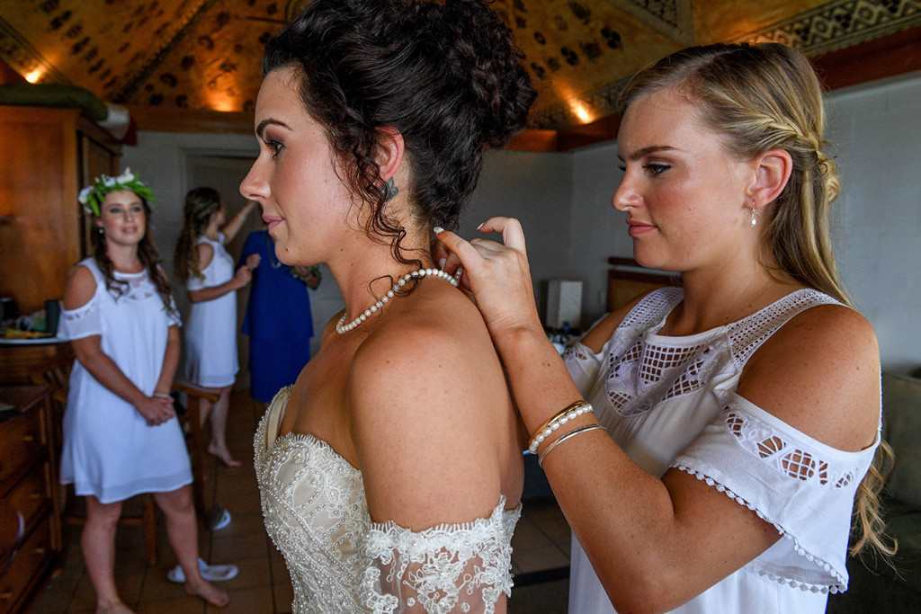 Mid closeup of bridesmaid putting pearl necklace on bride
