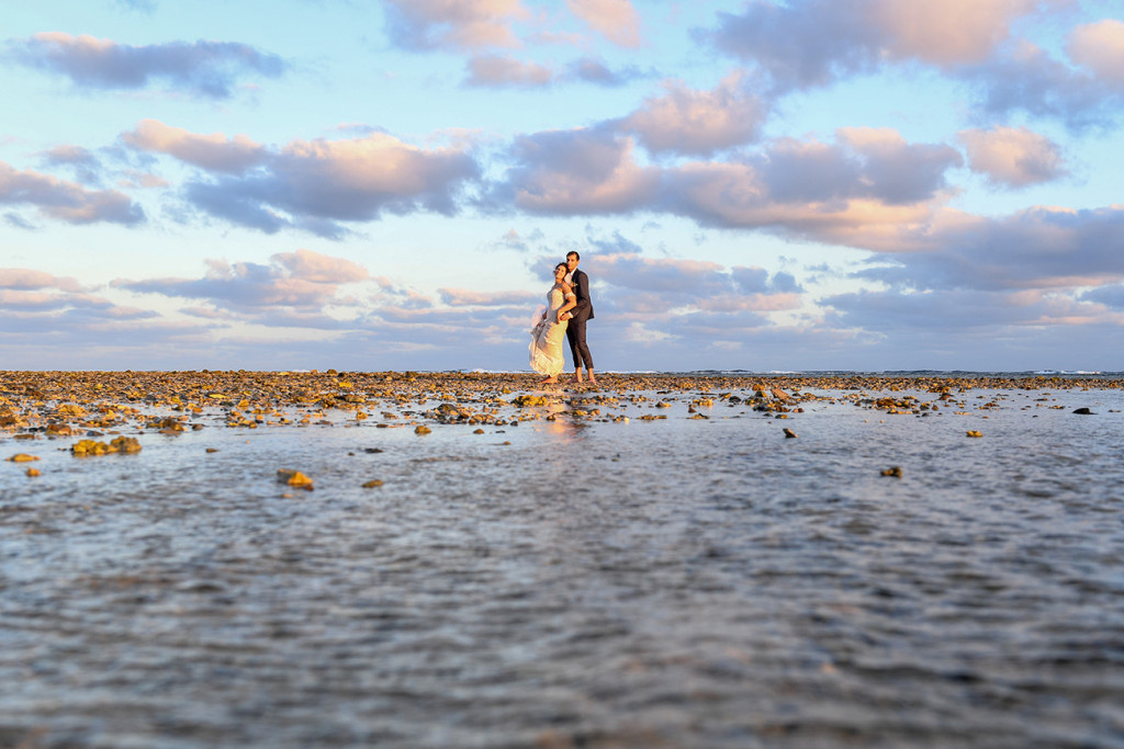 Wideshot of bride and groom in the ocean at sunset