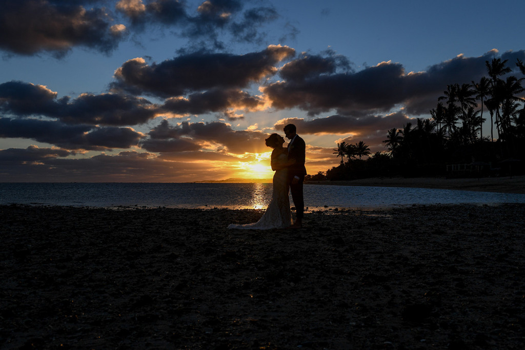 Wide silhouette of bride and groom kissing against sunset