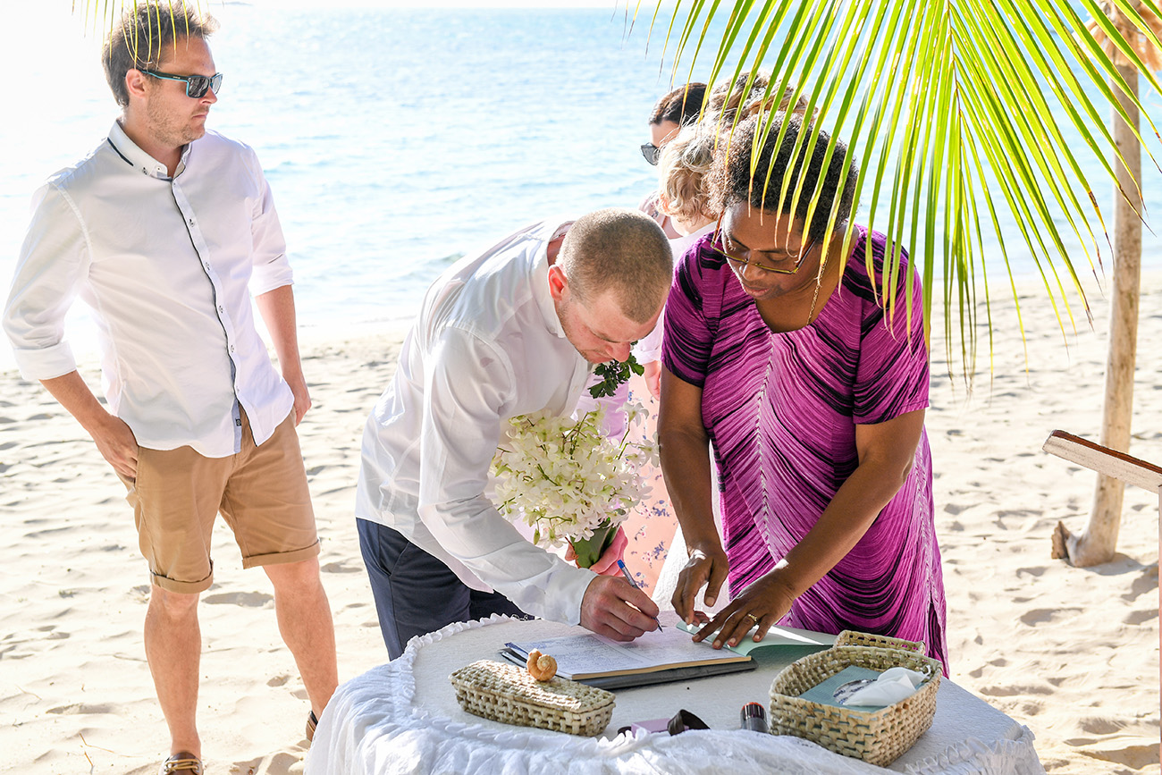 The groom signs the marriage certificate by the beach in front of witnesses