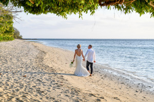 Wideshot of bride and groom strolling hand in hand on the Plantation Island Resort Beach