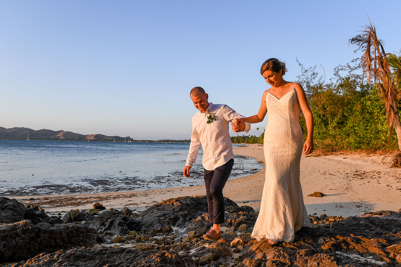 Groom helps his bride over a rock at the Plantation Island Resort Fiji