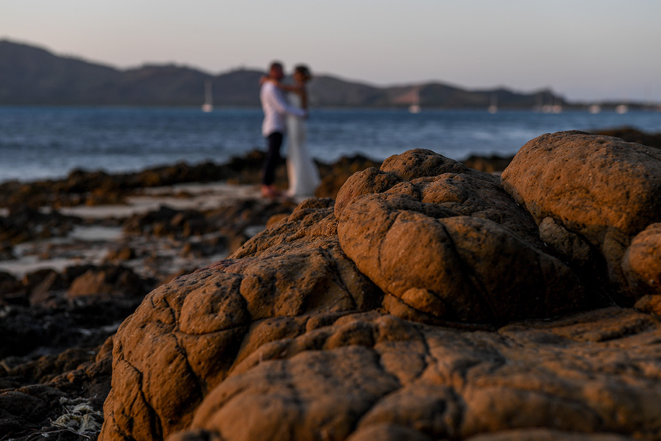 Coral rock in the foreground as Bride and groom dance on coral rocks against the sea