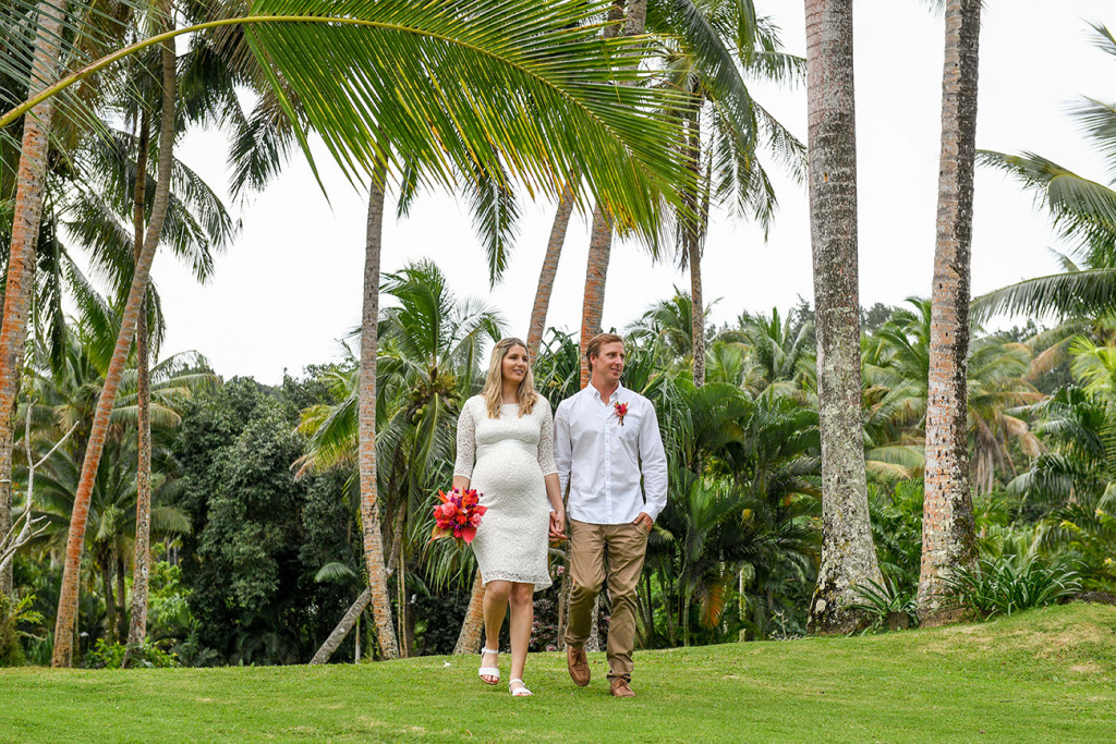 The pregnant bride and groom are walking among the palm trees at the Warwick Fiji