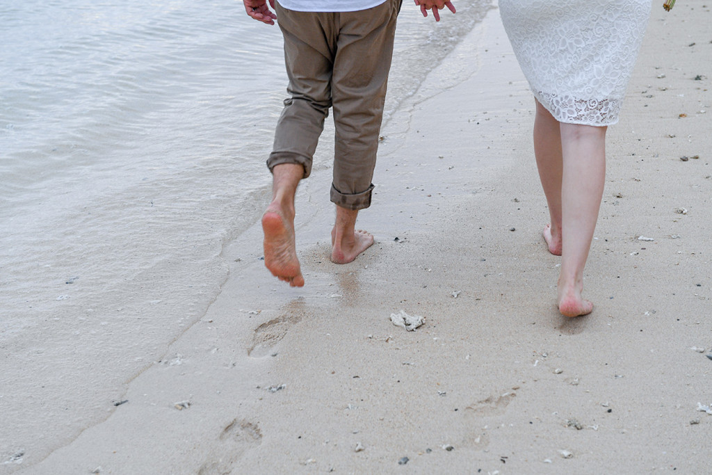 Bride and groom walking bare feet along the beach with clear water in Fiji