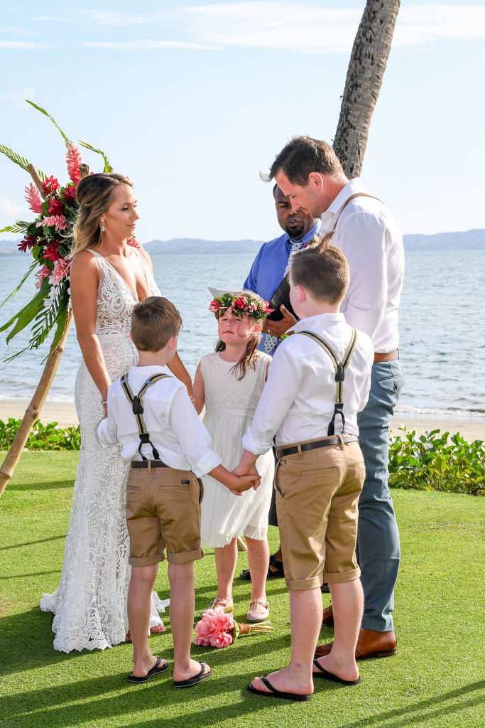 The bride, groom and children hold hands at the altar overlooking breathtaking Fiji beach