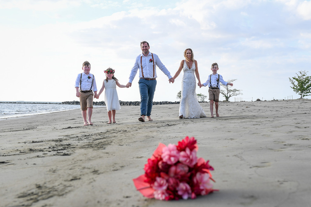 Pink flower bouquet in foreground of family photo at black sand beach