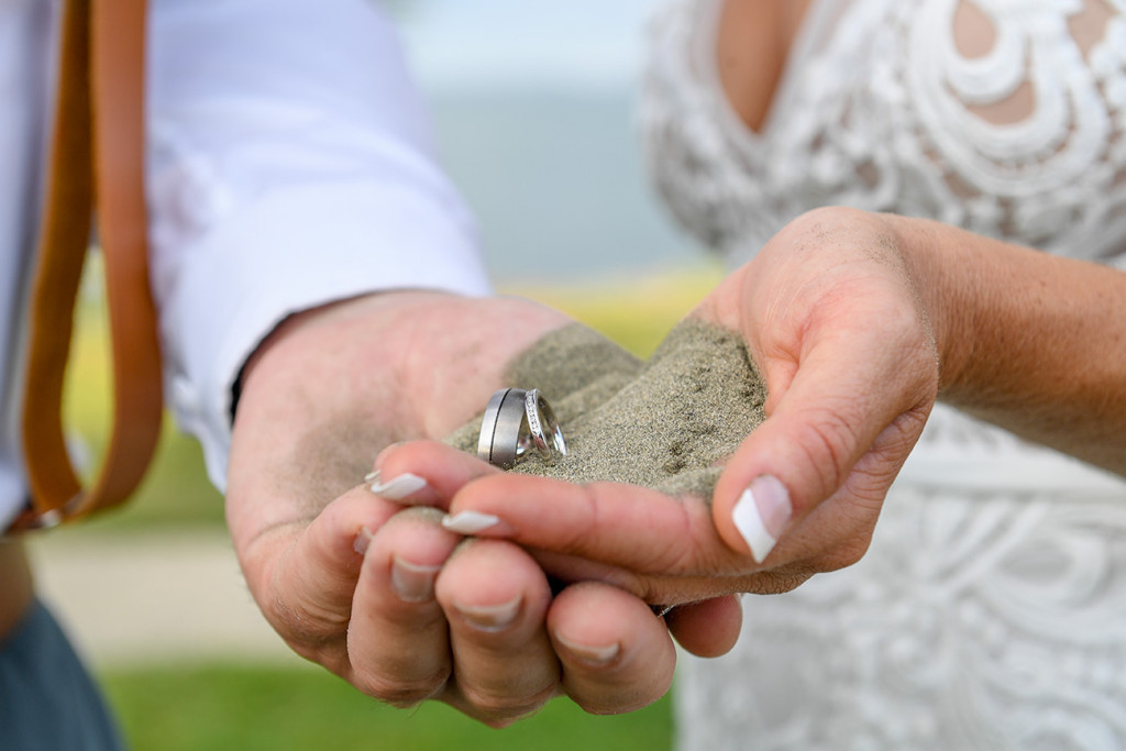 Bride and groom cup their silver and diamond rings in black sand