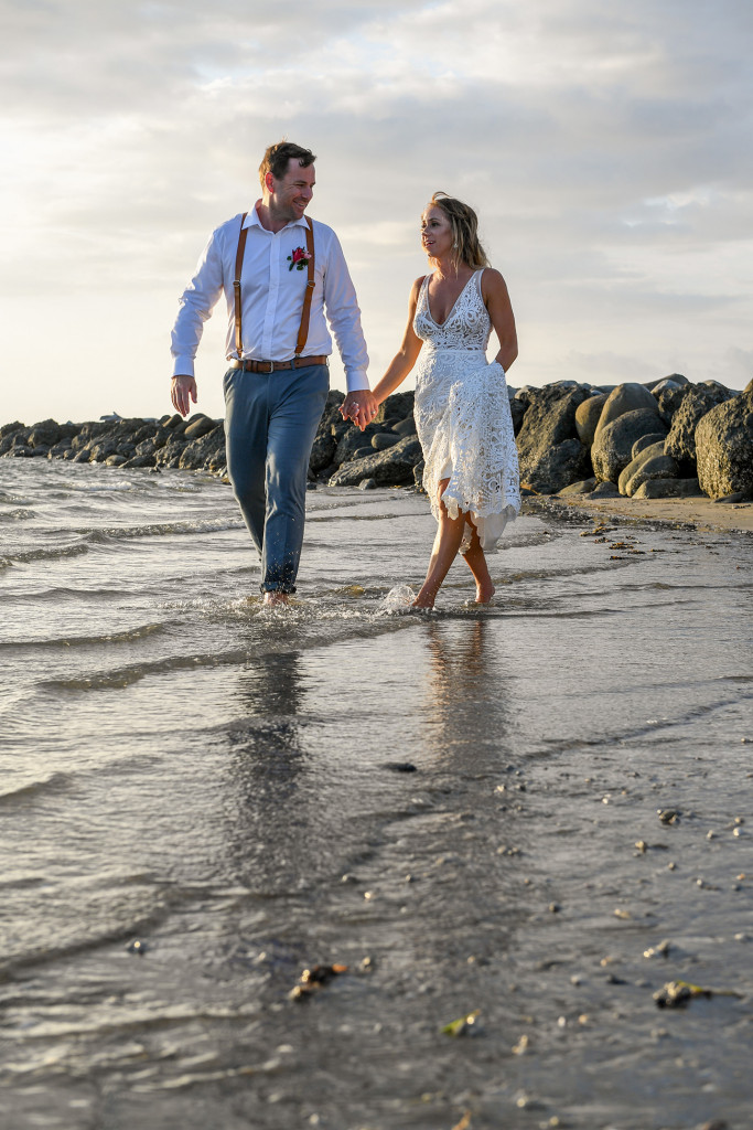 Bride and groom stroll in the shallow waters of the Pacific ocean at sunset in Fiji