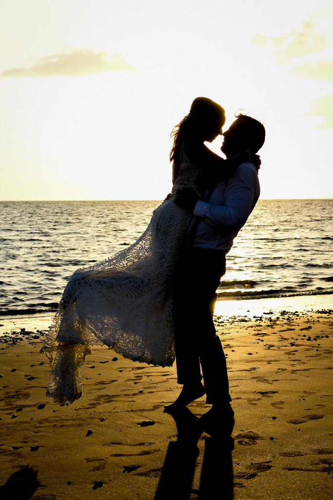Silhouette of Groom lifting bride against golden Fiji sunset