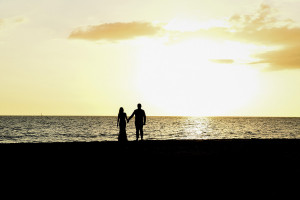 Silhouette landscape photo of bride and groom walking into the sunset of the Pacific ocean