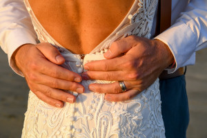 Closeup of the groom's hands holding his bride's waist in the amber glow of sunset