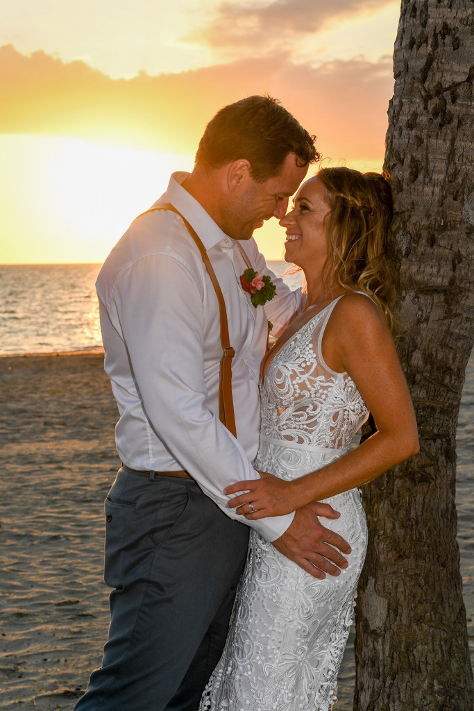 Bride and groom embrace against a palm tree in the golden sunset