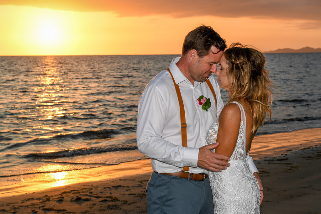 The bride and groom have a moment against the golden sunset over the Pacific ocean