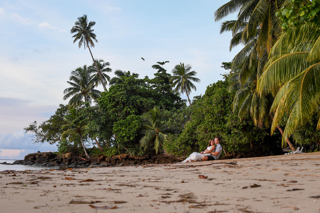 Engaged bride and groom sited on the beach looking at the sea, Matangi Island resort, Fiji