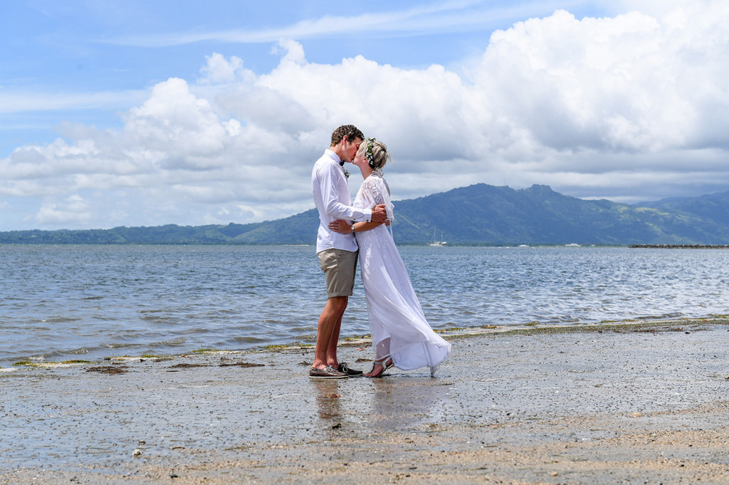 The newly married couple kisses while standing in the awe-inspiring Pacific ocean at their destination wedding