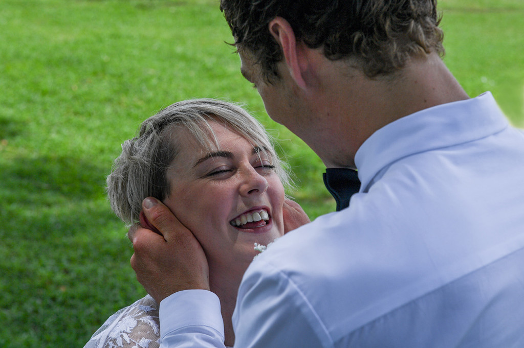 The bride laughs as the groom cups her face in his hands