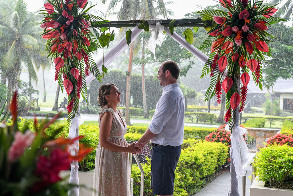 Bride and groom laugh at the tropical red flower altar
